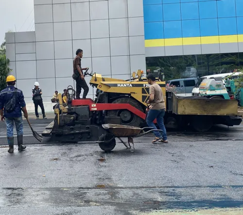 proses pengaspalan jalan menggunakan aspal curah dengan alat berat dan pekerja konstruksi